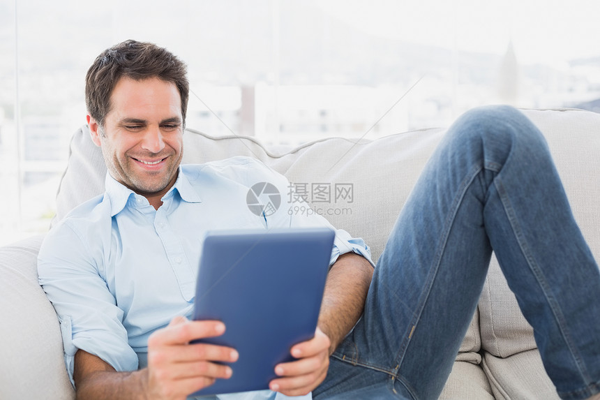 微笑的男人用平板电脑在沙发上放松图片