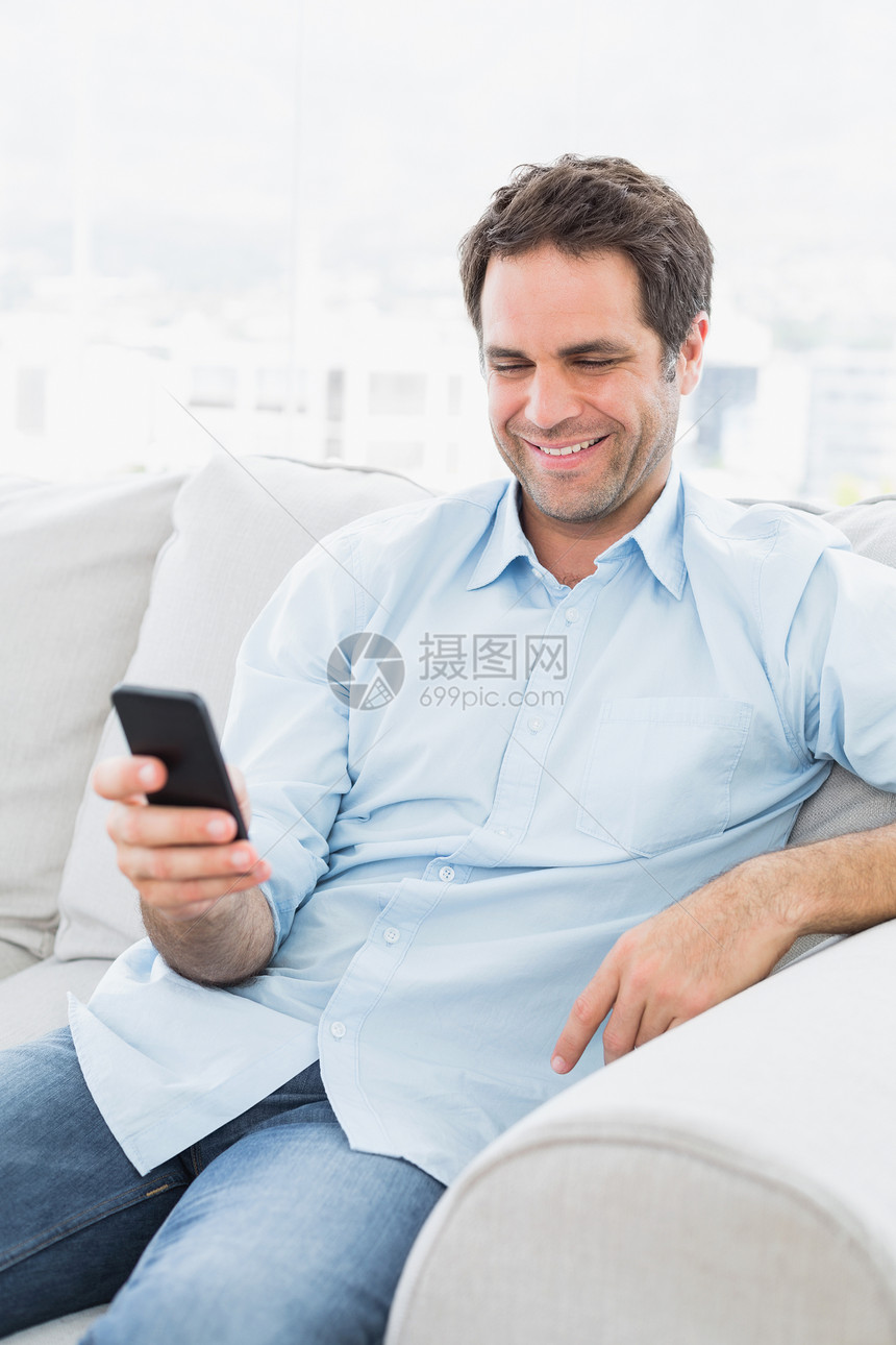 坐在沙发上欢快的男人 用智能手机发短信图片