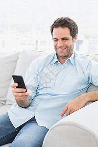 坐在沙发上欢快的男人 用智能手机发短信背景图片