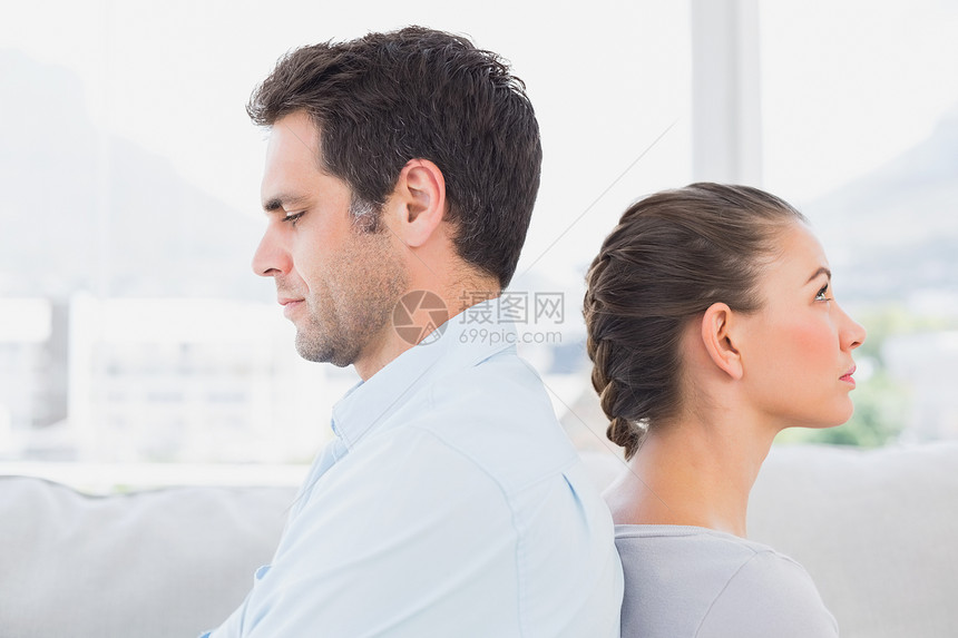 坐在沙发上背靠背坐着不快乐的一对情侣男人公寓女性长椅客厅女士男性房子家庭住所图片