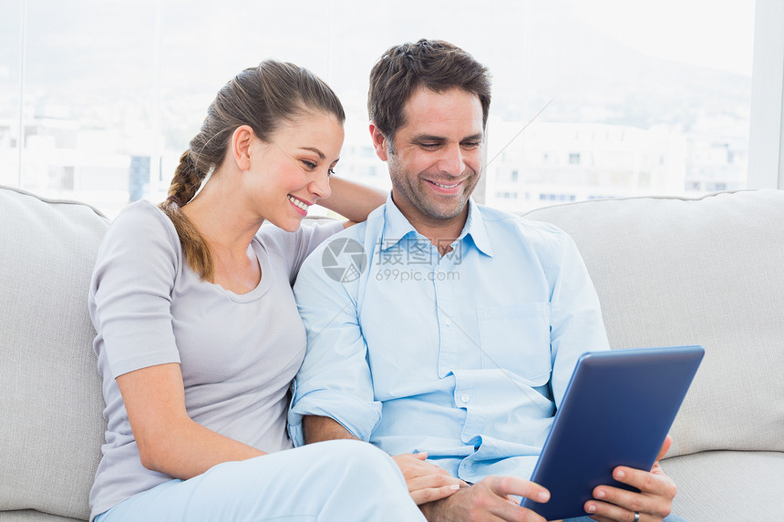 使用平板电脑坐在沙发上的微笑夫妇图片