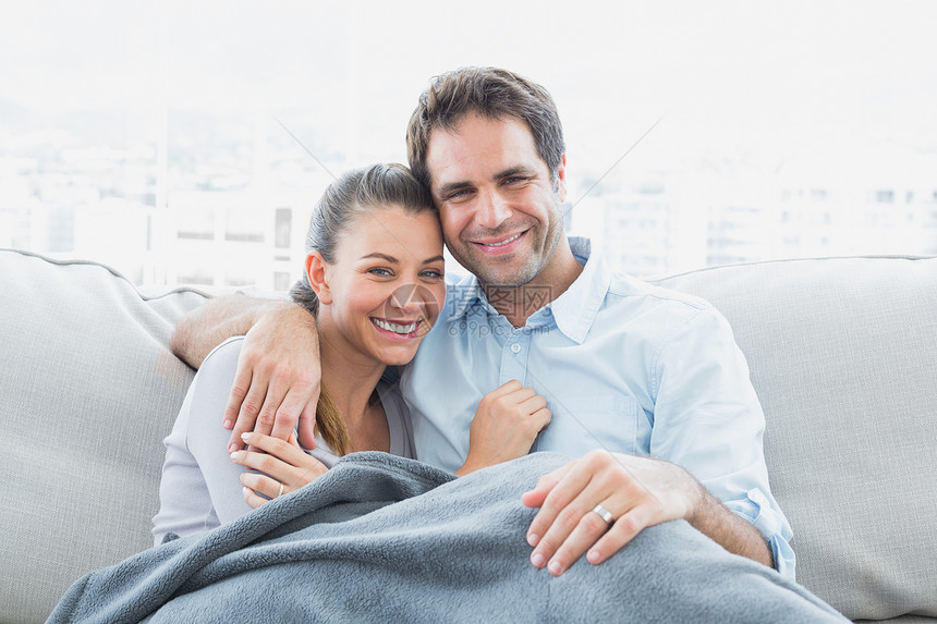 一对快乐的情侣在沙发上放松 笑着用毯子拍镜头图片