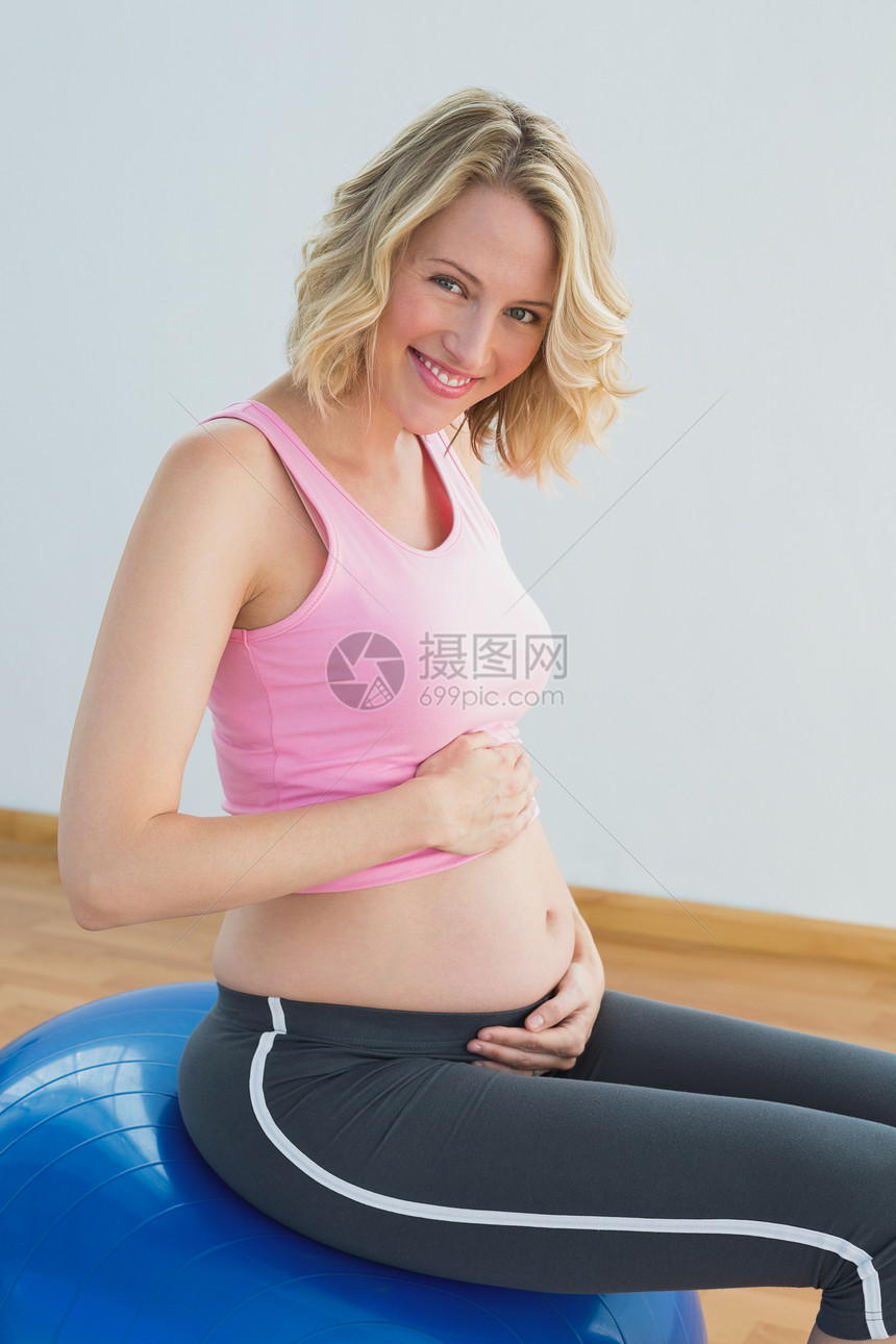 微笑的金发女怀孕妇女触摸锻炼球肚子图片
