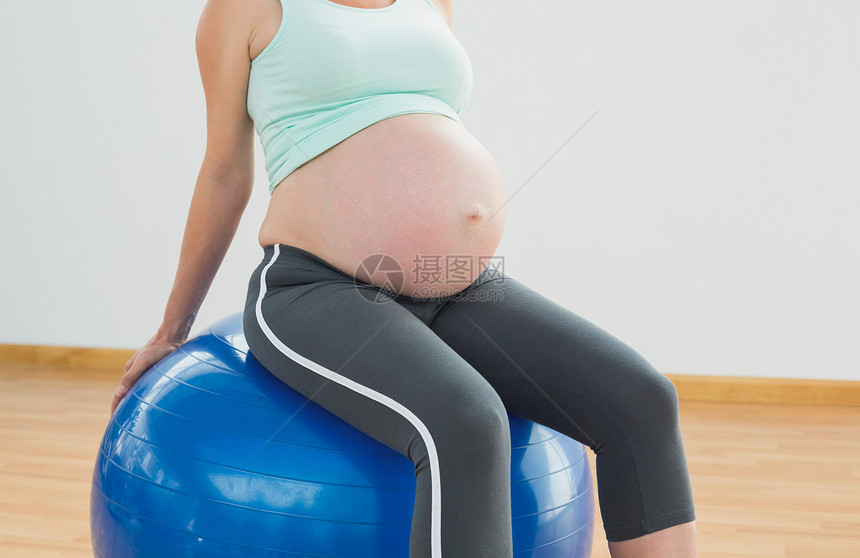 坐在蓝色运动舞会上的怀孕妇女腹部闲暇健身室运动服身体健身待产护理健身房男人图片