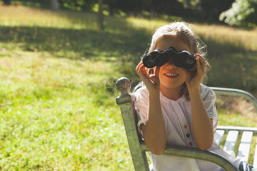 女孩在公园通过望远镜看望乐趣闲暇绿地好奇心勘探童年冒险绿色头发女性图片