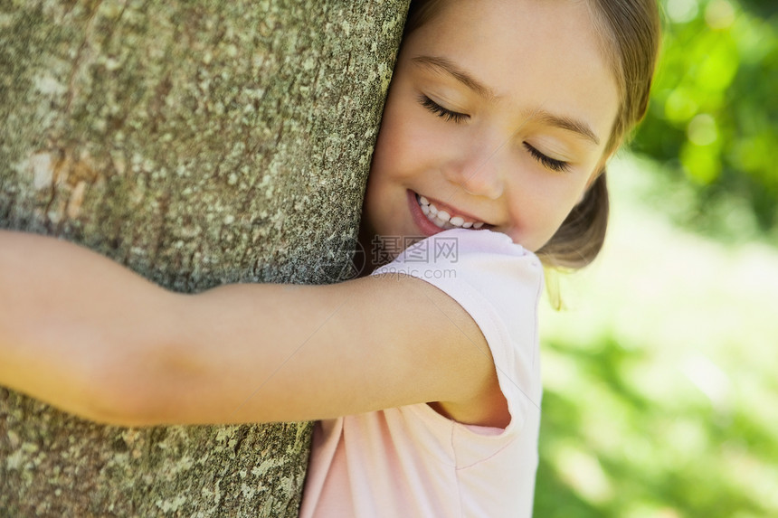 在公园闭着眼睛拥抱树的微笑女孩图片