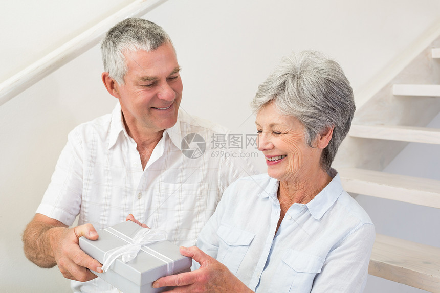 老人给快乐的伴侣送礼物客厅微笑女士住所闲暇女性头发岁月亲密感退休图片
