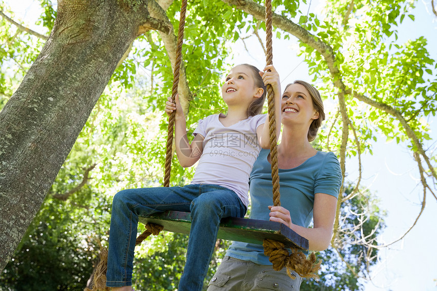 快乐的母亲在公园的摇摆女儿草地公园家庭母亲幸福女士快乐闲暇女性树木图片