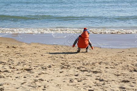 无袖外套孩子在沙滩上寻找石块背景