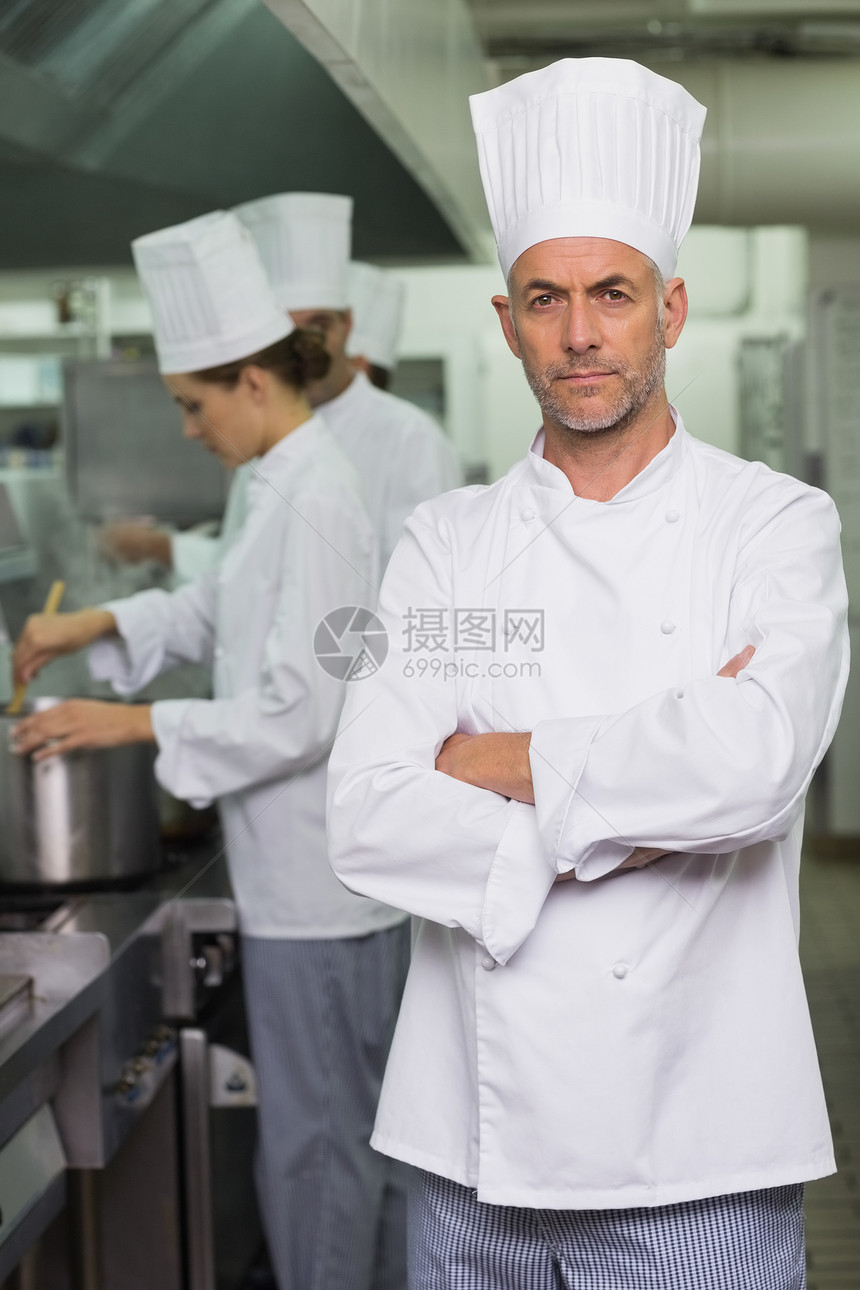 认真的厨师看着摄影机 团队在后面工作男性职业炉顶女性搅拌烹饪职员白人厨房伙伴图片