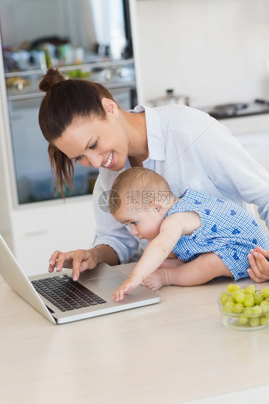 有婴儿的母亲在柜台使用笔记本电脑图片