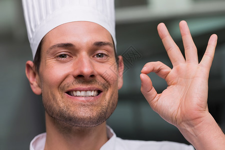 开心的厨师在相机上签好牌白人餐厅手势大楼餐饮厨房男人快乐制服工作背景