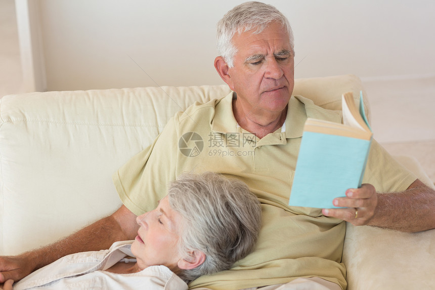 高级男子坐在沙发上与伴侣一起在大腿上休息阅读微笑文学成人客厅长椅退休感情男性住所说谎图片