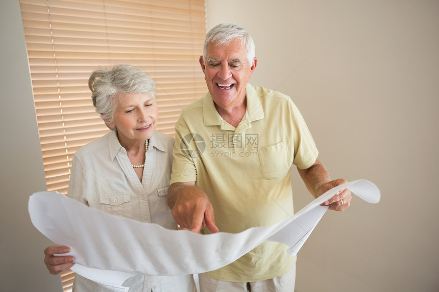 一起看房子蓝图的老夫妻情侣住所微笑老年退休屋主客厅夫妻家庭阅读成人图片