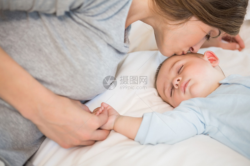 母亲在床上亲吻睡觉的婴儿儿子图片
