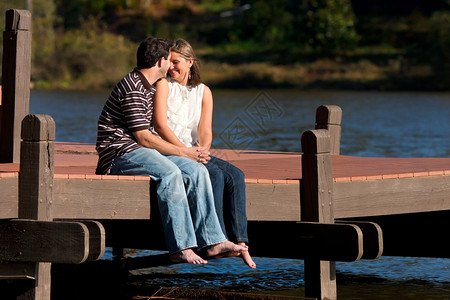 坐在湖码头赤脚边的小情侣共享亲密时刻背景图片