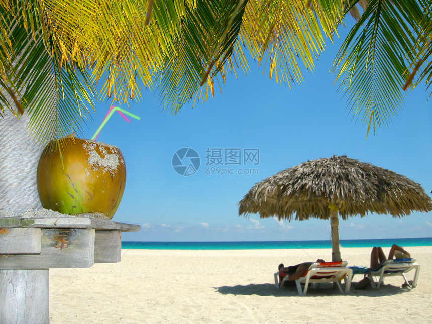 在热带海滩上放松人们海岸线小屋假期阴影海洋天堂棕榈旅游蓝色饮料图片