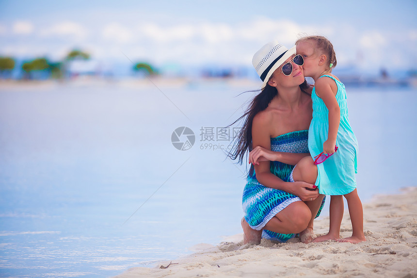 小女孩在白色热带海滩上亲吻她美丽的母亲的幼小女孩孩子海岸妈妈异国父母乐趣沙漠女孩女儿家庭图片