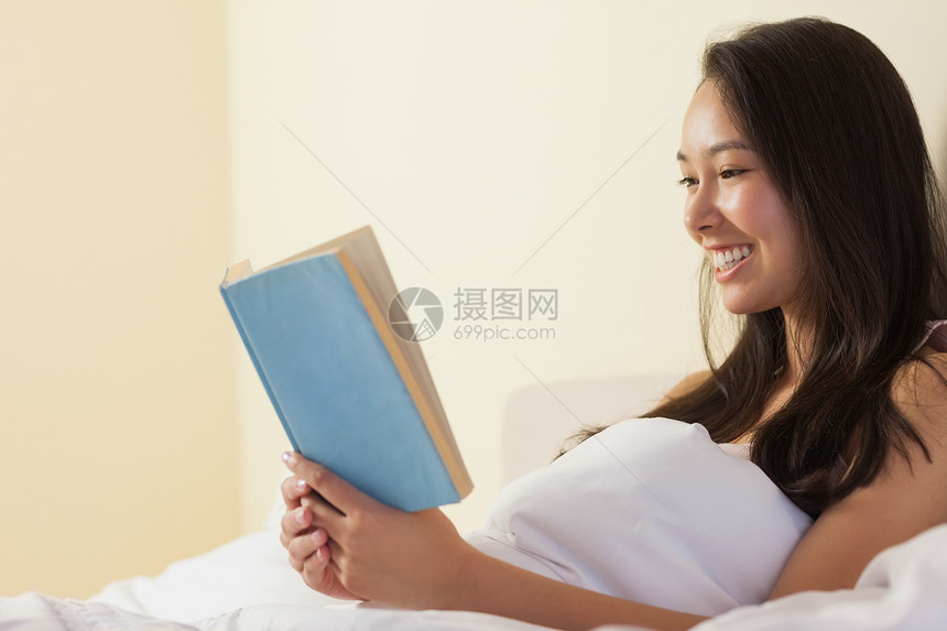 坐在床上看书的年轻快乐的年青女人图片