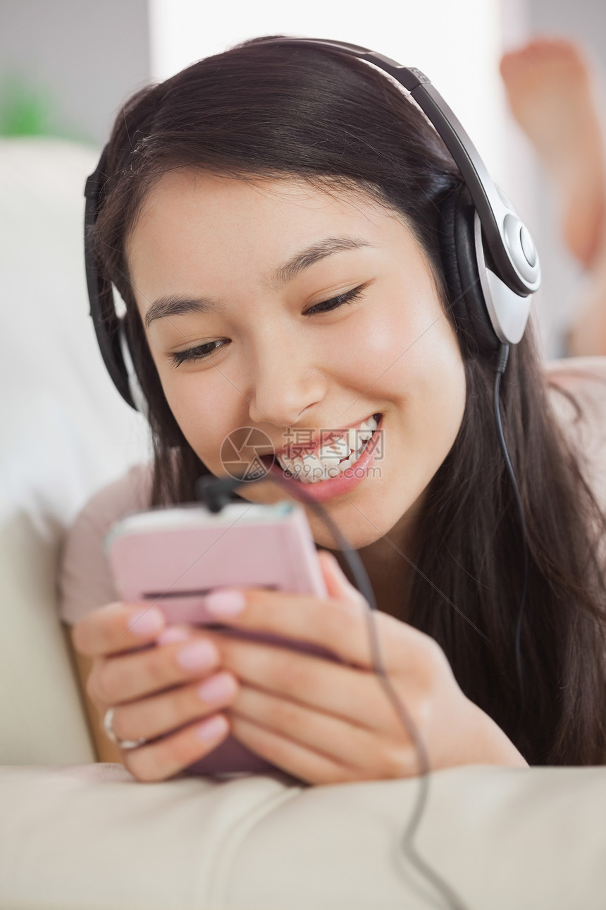 躺在沙发上 用智能手机收听音乐的欢乐的亚洲女孩图片