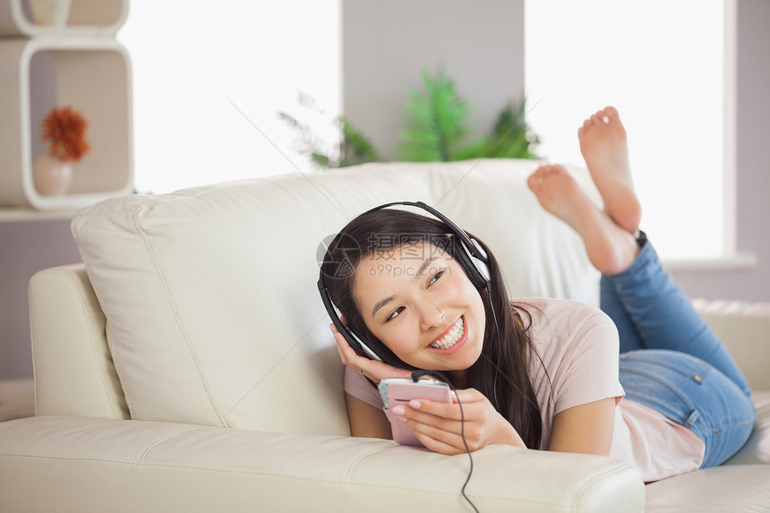 躺在沙发上微笑着的年轻女孩 用智能手机收听音乐图片