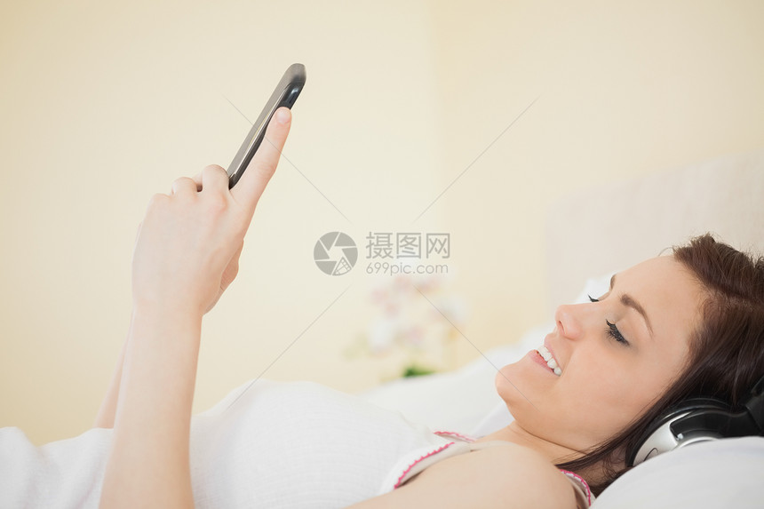 躺在床上的微笑女孩在她的智能手机上听音乐图片