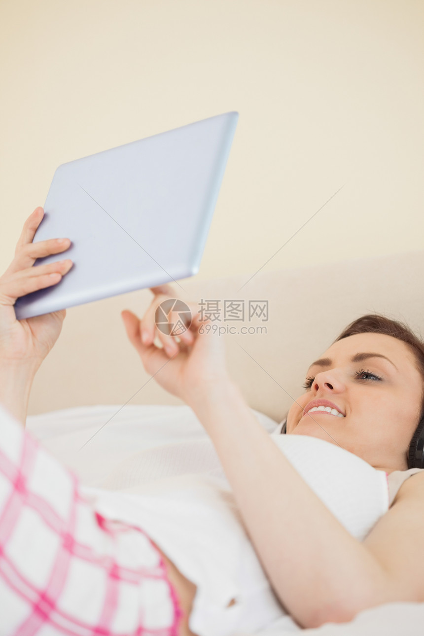 微笑的女孩拿着平板电脑躺在床上图片