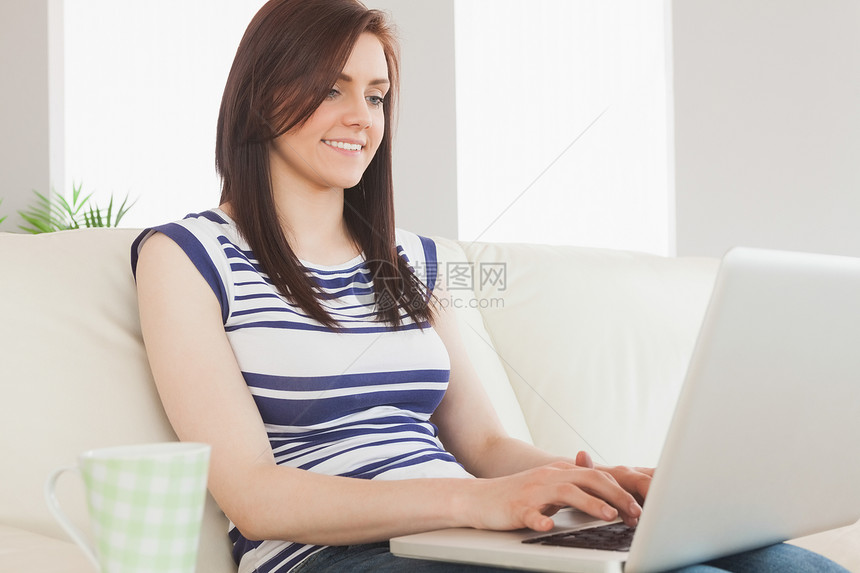 微笑的女孩用笔记本电脑坐在沙发上图片