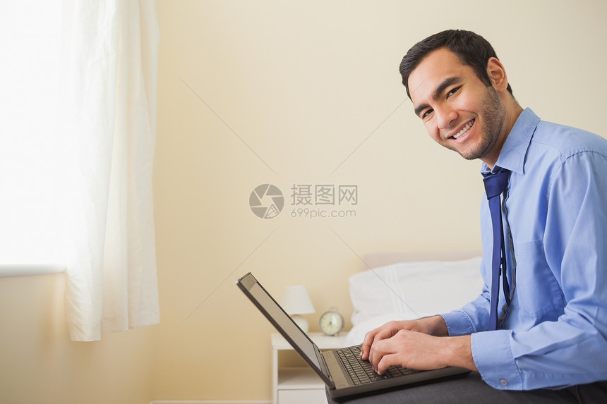 使用笔记本电脑坐在床上微笑的男人卧室混血商务窗帘短发领带技术男性头发黑眼睛图片