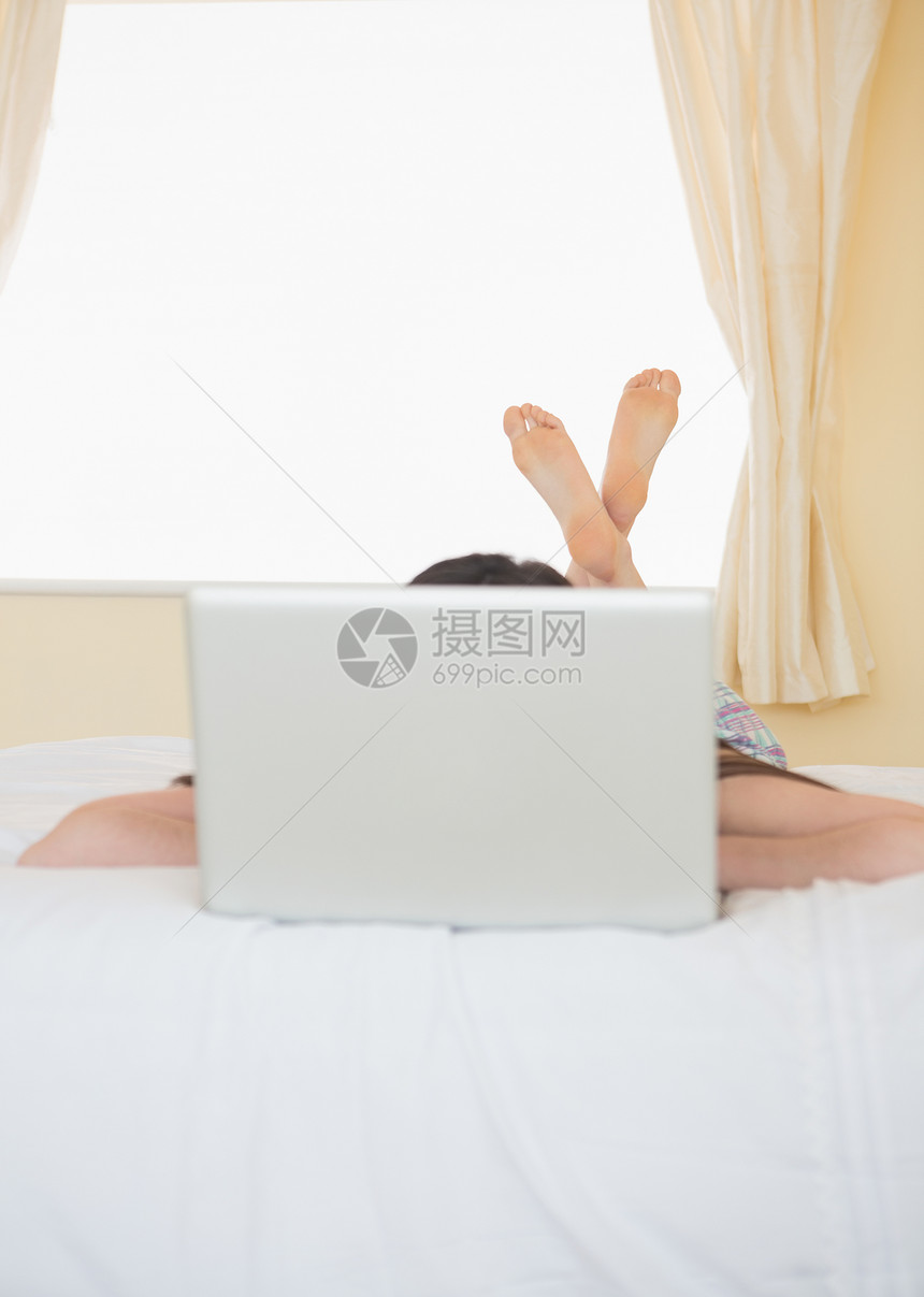 女孩躺在笔记本电脑后面的床上图片