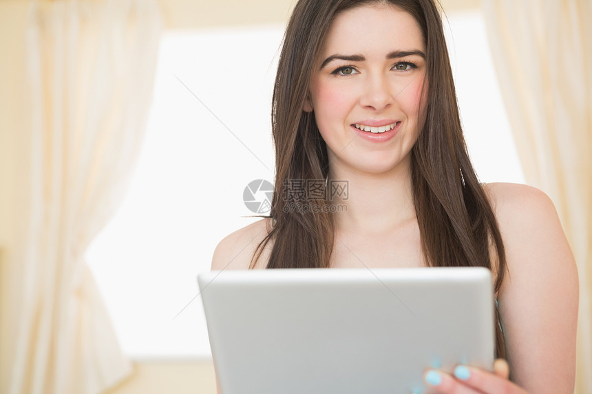 漂亮女孩看着相机 用平板电脑坐在床上看相片图片