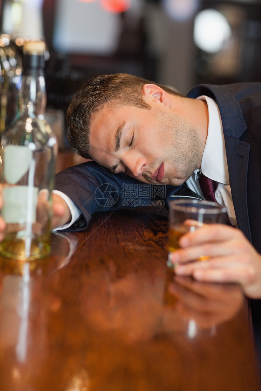 醉酒商务人士拿着威士忌杯 躺在柜台上图片