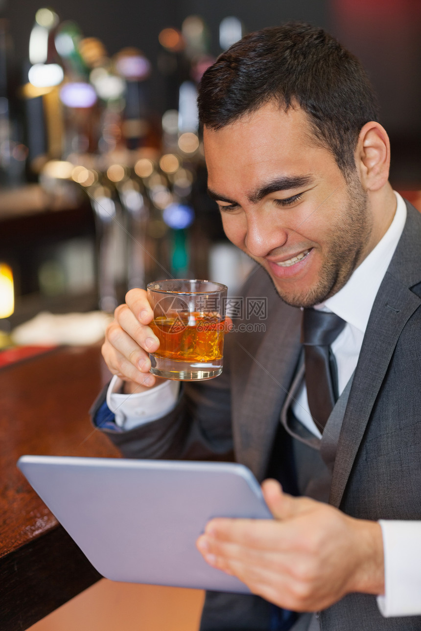 一边喝威士忌一边在平板上工作的笑脸商务人士图片