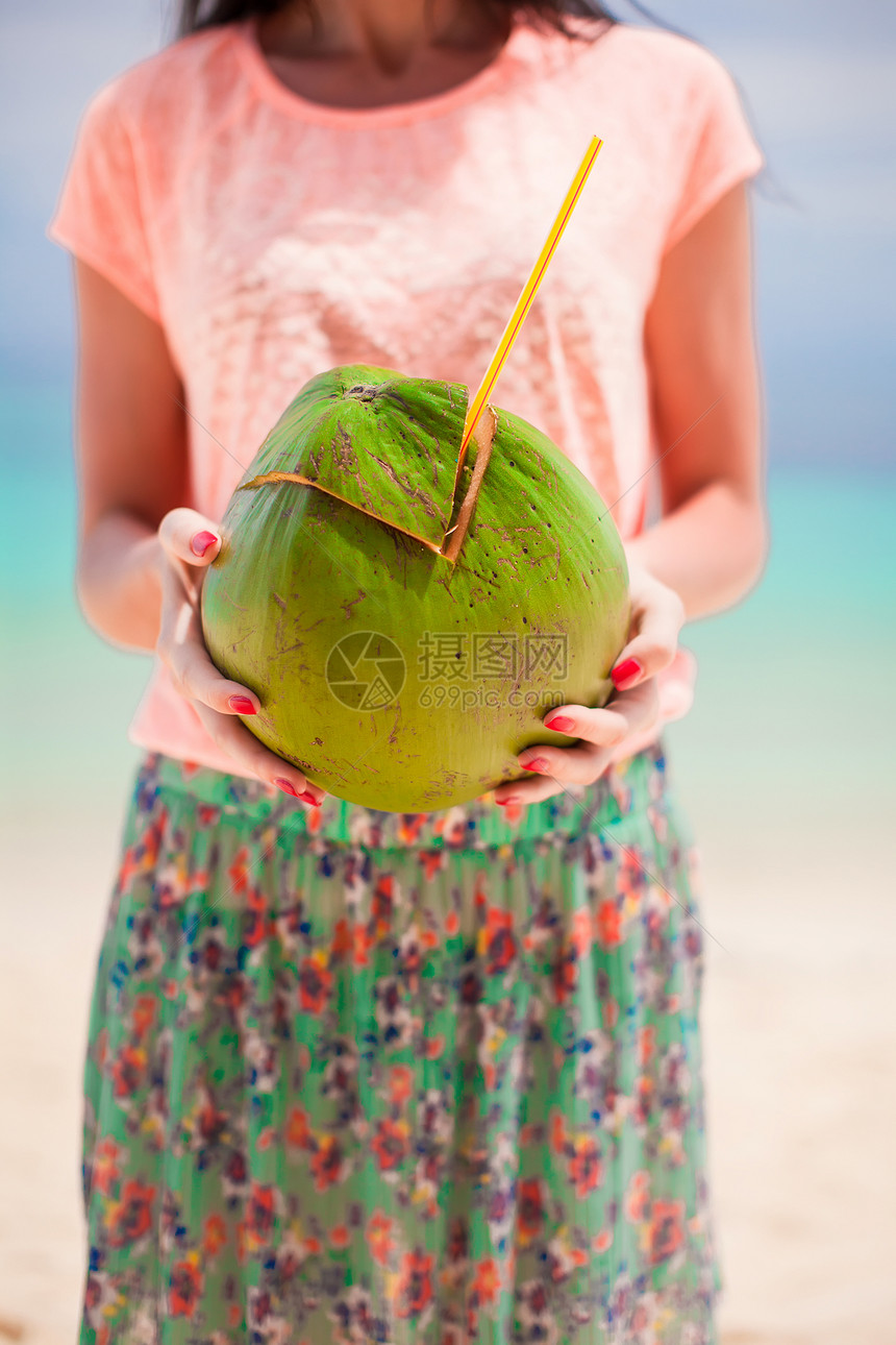 青绿大椰子放在年轻女子手中海岸情调海洋女孩牛奶女性蓝色热带海滩围裙图片