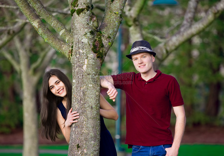年轻的跨种族夫妇站立在树上少数民族牛仔裤微笑女孩男人夫妻男生树干公园混血儿图片