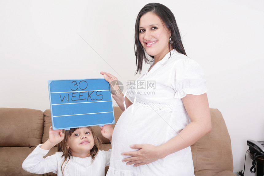 女孩拿着30周的标志给孕妇母亲看女士客厅生长沙发男生成人怀孕家庭生育力生活图片