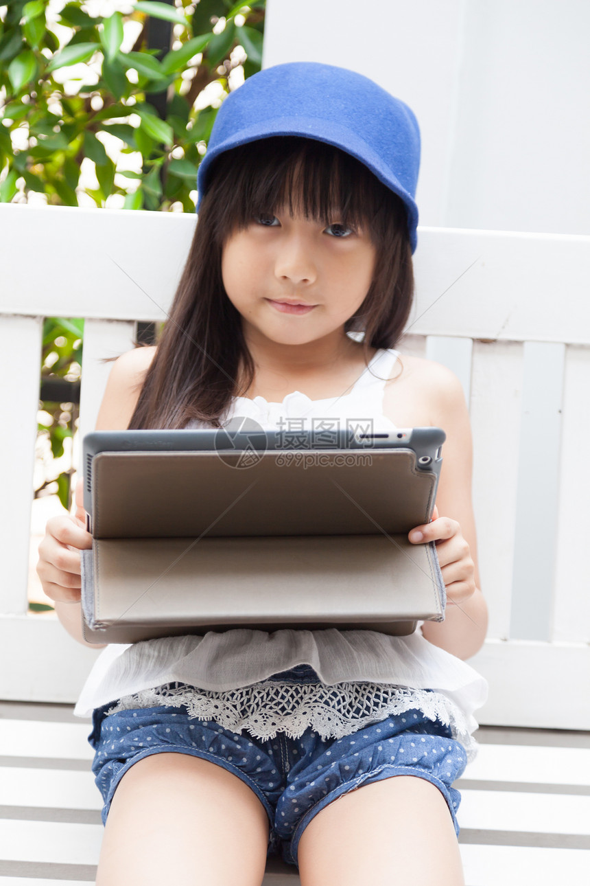 女孩在板凳上玩平板电脑孩子帽子沙发互联网房子长椅游戏屏幕通讯教育图片
