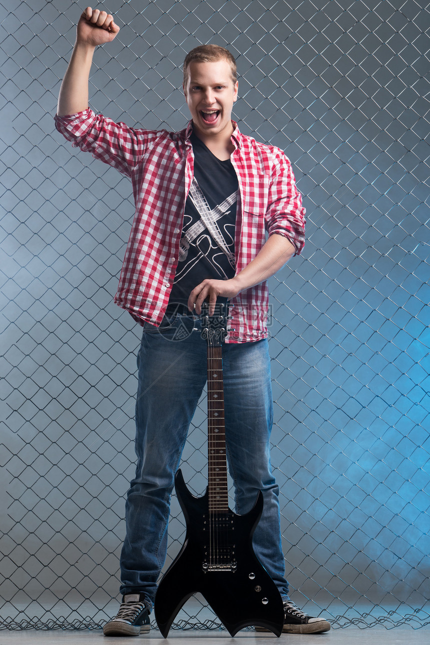 年轻音乐家 有一把吉他 在栅栏背景上金属吉他手摇杆衬衫蓝色欢呼旋律音乐演员衣服图片