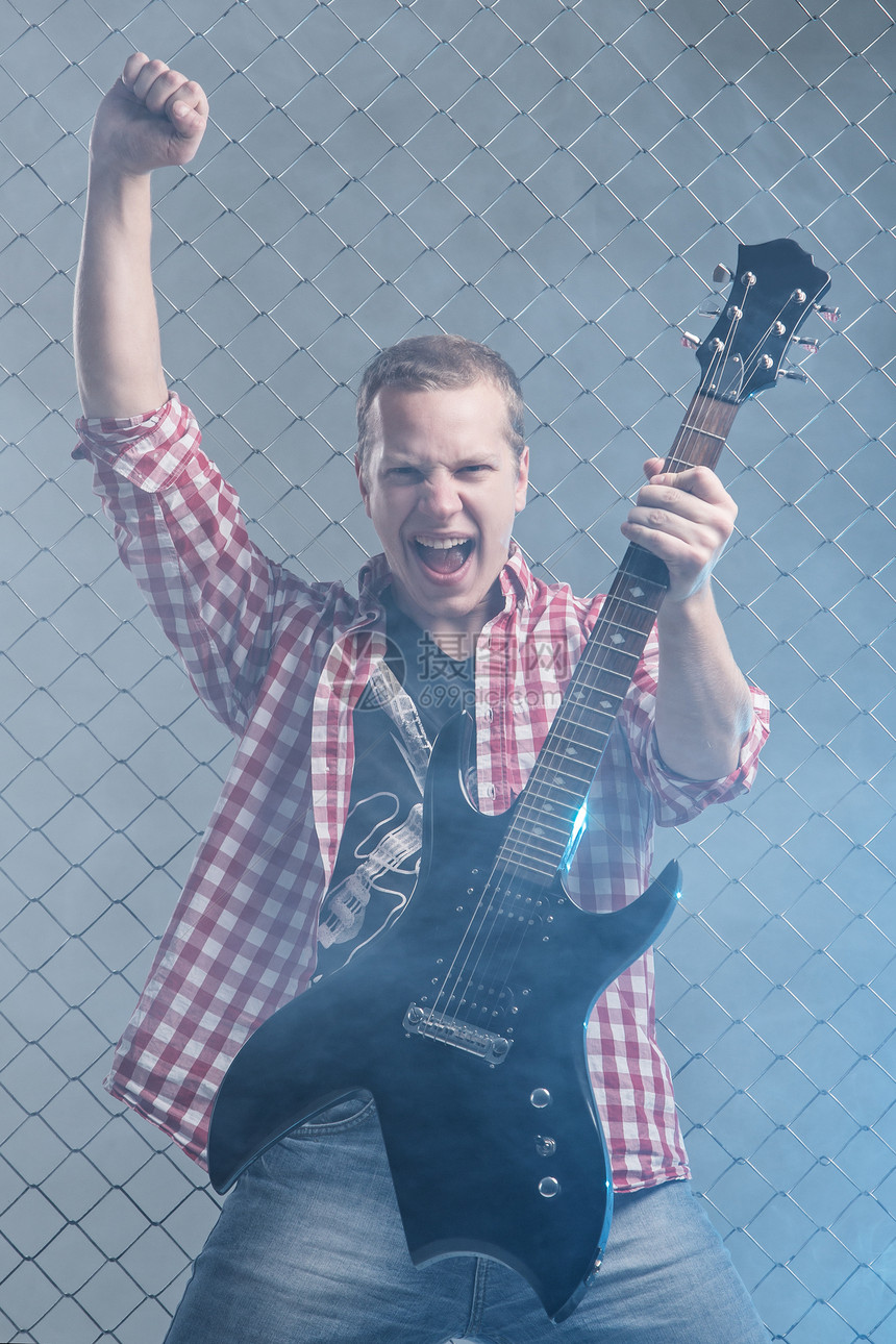 年轻音乐家 有一把吉他 在栅栏背景上金属男人岩石吉他手艺术家音乐会星星歌曲音乐牛仔裤图片