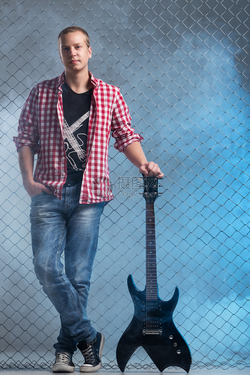 年轻音乐家 有一把吉他 在栅栏背景上金属岩石艺术家摇杆唱歌流行音乐音乐会星星蓝色衬衫图片