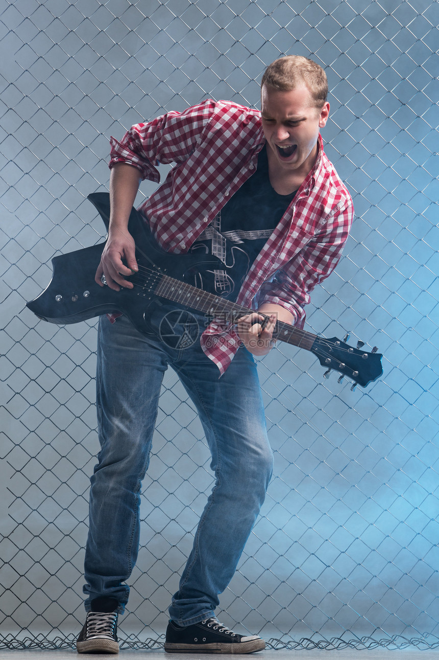 年轻音乐家 有一把吉他 在栅栏背景上蓝色衣服玩家岩石金属男人音乐尖叫摇杆娱乐图片