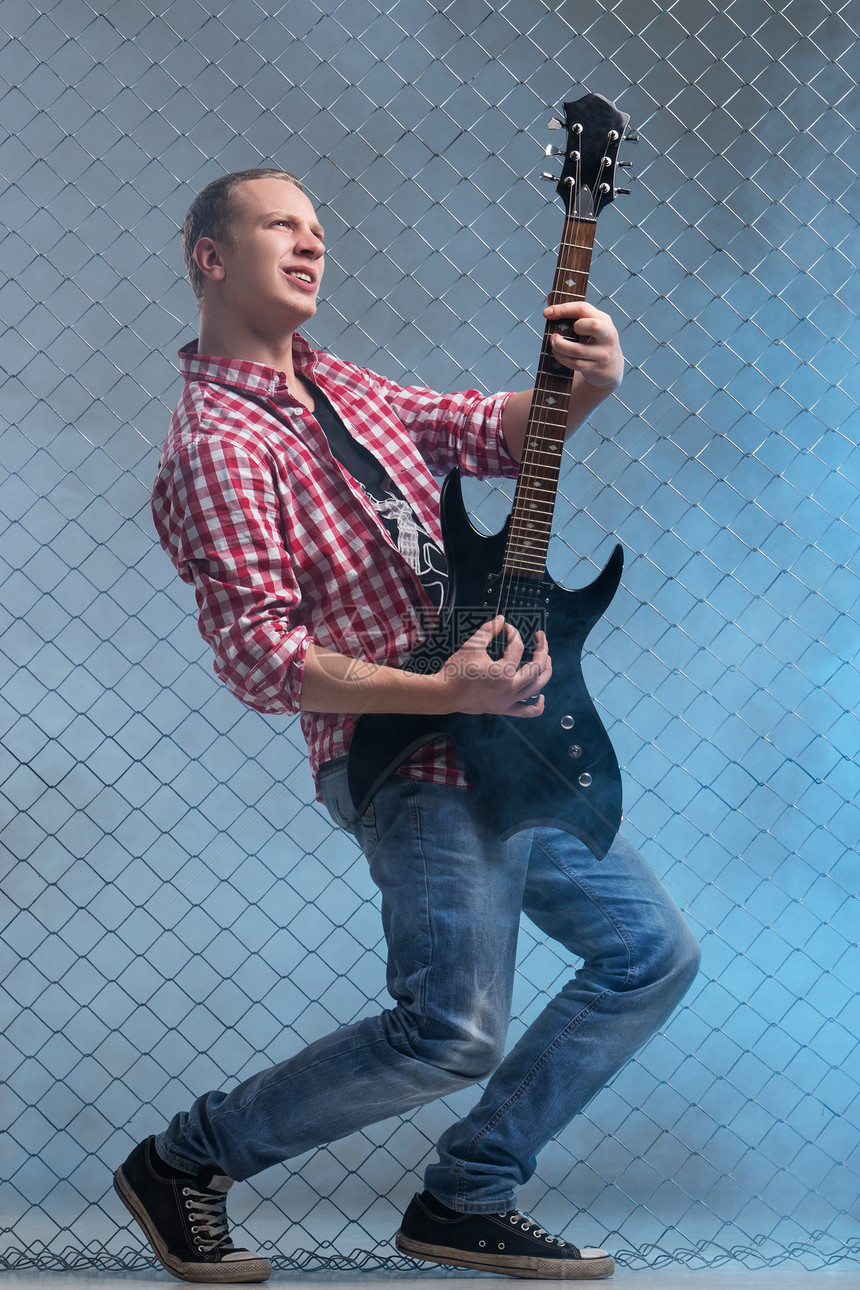 年轻音乐家 有一把吉他 在栅栏背景上旋律歌手蓝色摇杆玩家乐器唱歌岩石衬衫金属图片