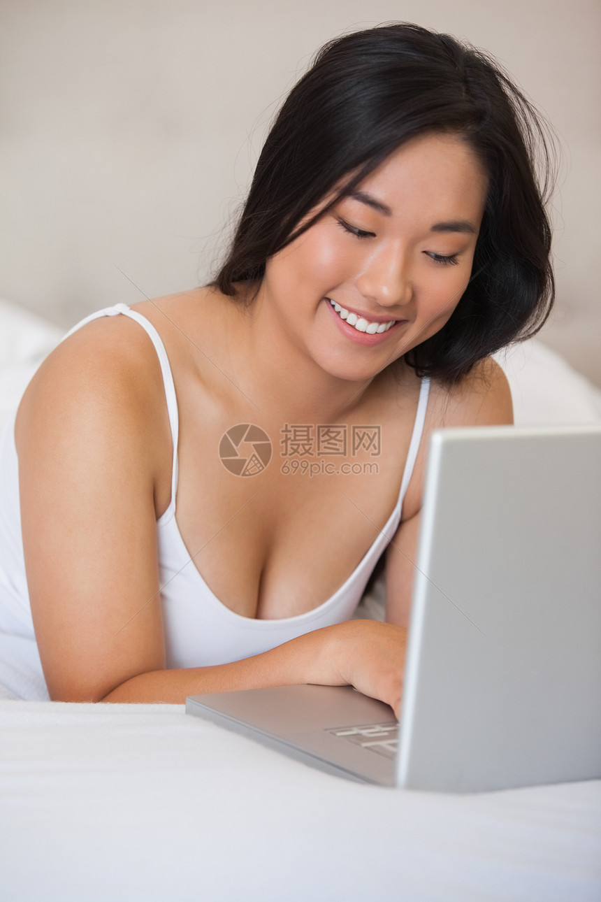 用笔记本电脑躺在床上的漂亮亚洲人图片