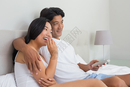 躺在床上看电视时笑着笑着的情侣电视遥控说谎男性黑发快乐享受家庭家庭生活娱乐性背景图片
