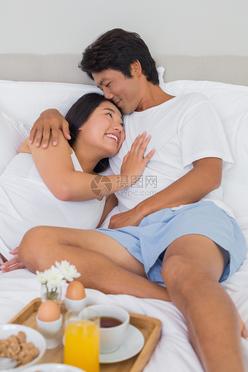 幸福的情侣在床上吃早餐拥抱闲暇男性快乐睡衣托盘羽绒被家庭家庭生活感情图片