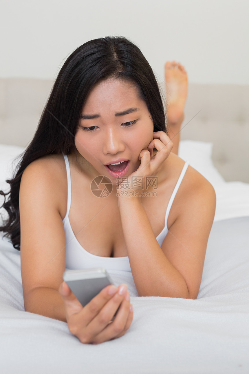 躺在床上拿着智能手机的惊吓女人图片