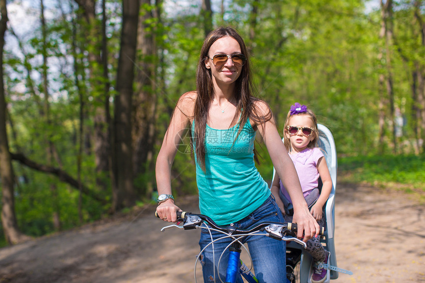 年轻母亲和可爱的小女儿一起骑自行车 同时骑自行车图片