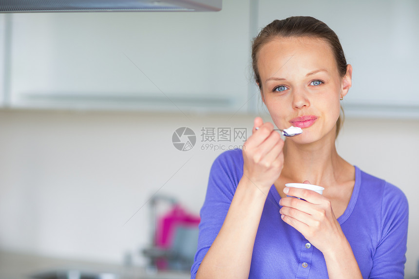 快乐的年轻女子在厨房吃酸奶茶匙奶制品美食勺子青年房子小吃女性甜点牛奶图片