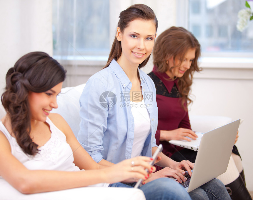三个女孩和一台笔记本电脑学生沙发说谎房间工作网络互联网快乐微笑女孩们图片