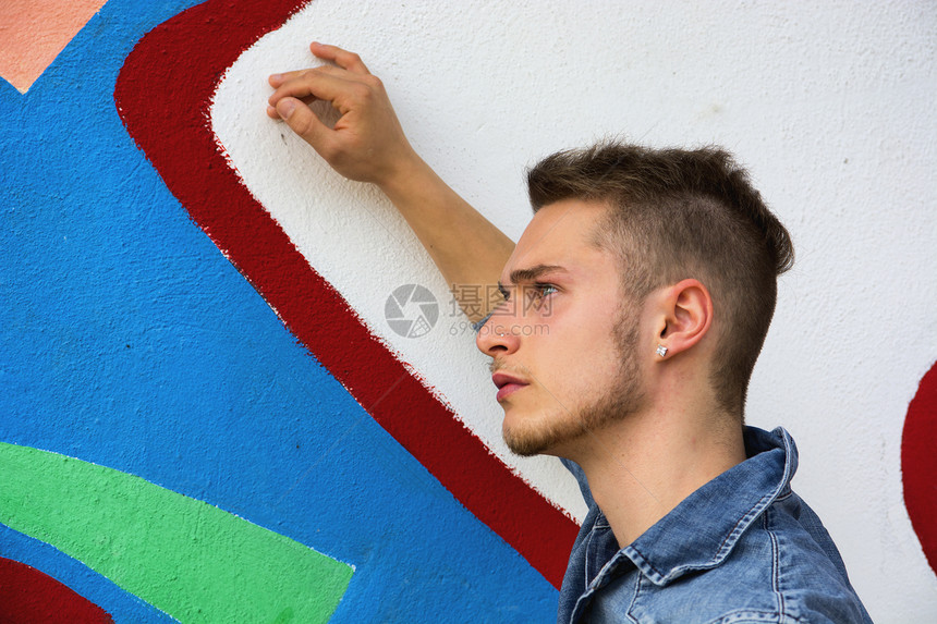 金发英俊的年轻男子 对抗色彩多彩的涂鸦墙壁头发男生衬衫牛仔布城市乐趣男性成人街道男人图片